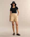 A person wearing a black short-sleeve shirt, the Newport Short, black sandals, and a black bucket hat stands against a plain beige background.