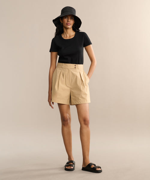A person wearing a black short-sleeve shirt, the Newport Short, black sandals, and a black bucket hat stands against a plain beige background.