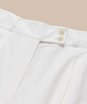 Close-up of the waistband and upper section of the Newport Trouser in white cotton poplin, with two beige buttons and pleated details, shown against a light beige background.