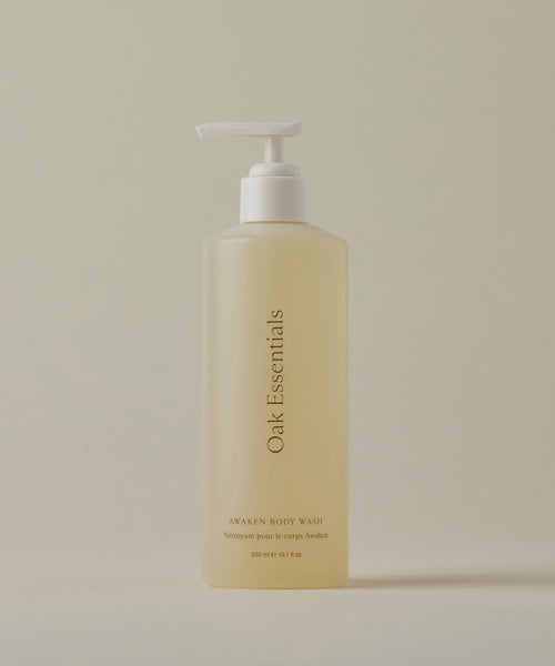 A translucent bottle with a white pump, labeled Awaken Body Wash, is displayed against a plain, light beige background.