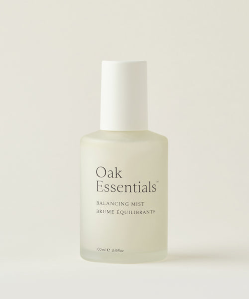 A frosted glass bottle of Balancing Mist with aloe leaf juice and rose water, topped with a white cap, is set against a plain light background. The minimal label features black text.