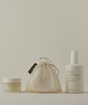 The Double Cleanse Set, featuring a Cleansing Balm and Pure Gel Cleanser in a mesh drawstring bag, is arranged against a neutral background for a hydrated complexion.