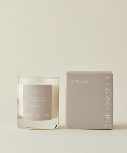 A Violet Santal Candle, with a minimalist light design, is set against a neutral backdrop that reflects coastal nostalgia and the calming spirit of California woods.