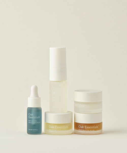 The Mini Routine by Five Oak Essentials features a dropper bottle, pump bottle, and three jars in various sizes with white and amber accents—perfect travel skincare companions arranged on a neutral background.