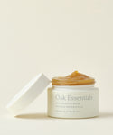 An open jar of Restorative Mask with its white lid beside it displays the golden, gel-like mask, enriched with Avocado Oil and organic honey, set against a plain light background.