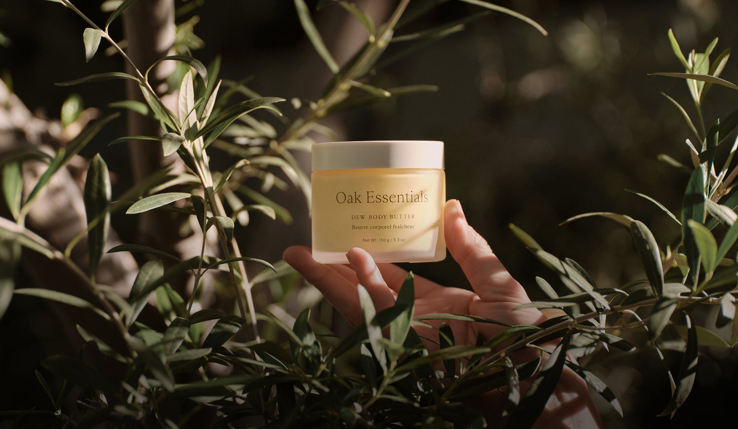 Hand holding a jar of 'Oak Essentials' product among green leaves