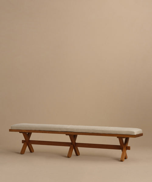 The Outdoor Garden Dining Bench features a minimalist solid teak frame, a cushioned seat in light beige Tempotest fabric, and crossed legs, displayed against a plain beige background.