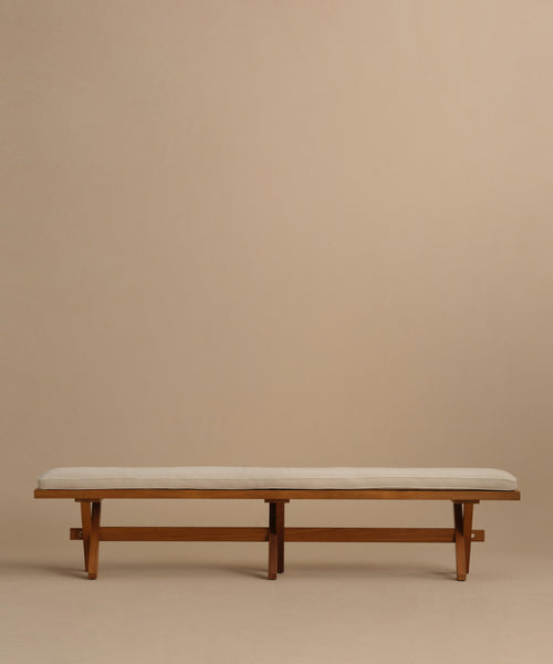 The Outdoor Garden Dining Bench features a minimalist solid teak frame, simple lines, and a light beige Tempotest fabric cushion. Set against a plain beige background, this sturdy bench offers comfort and style for any outdoor space.