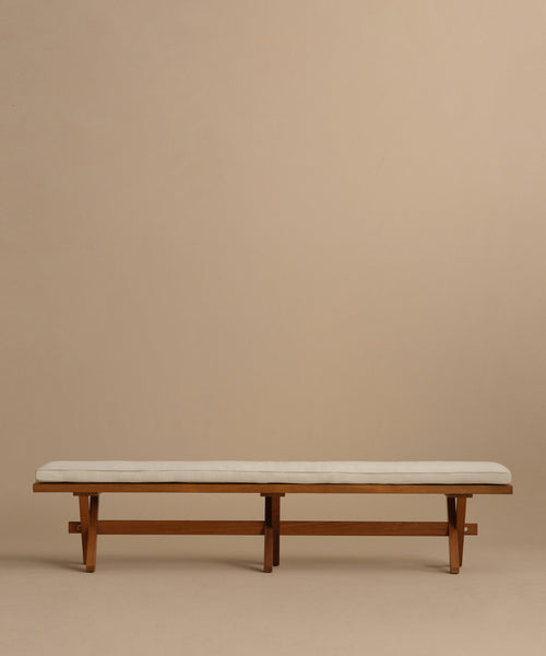 The Outdoor Garden Dining Bench, featuring a minimalist solid teak design and a light Tempotest fabric cushion, is set against a plain beige background.