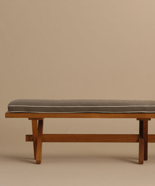 The Outdoor Garden Dining Bench features clean lines, tapered legs, and a simple solid teak design. It includes a rectangular gray Tempotest fabric cushion on top with a beige background.