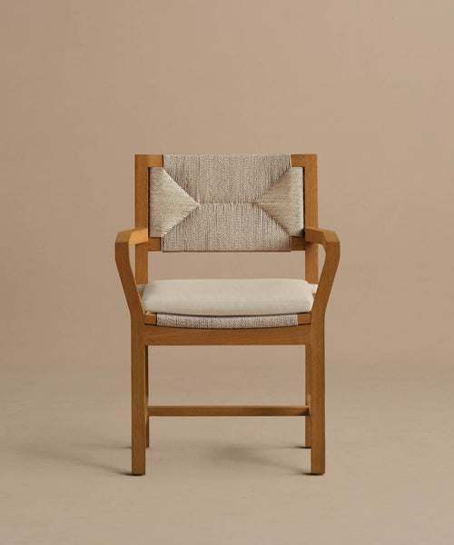 The Outdoor Montecito Dining Arm Chair features a solid teak frame, a light beige geometric woven backrest, and a Tempotest fabric cushion, shown here against a plain taupe background.