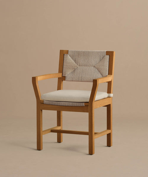 The Outdoor Montecito Dining Arm Chair features a beige Tempotest fabric cushion and a textured patterned backrest, showcased against a plain light brown background.