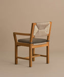 The Outdoor Montecito Dining Arm Chair features a solid teak light brown frame, gray cushioned seat, and ECOLENE woven beige backrest, shown against a neutral beige background.