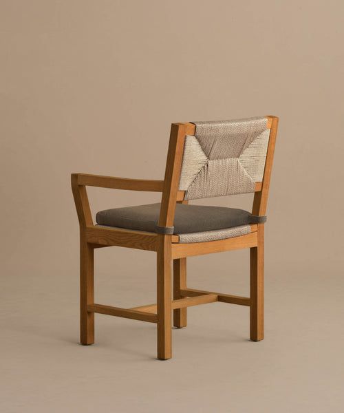 The Outdoor Montecito Dining Arm Chair features a solid teak light brown frame, gray cushioned seat, and ECOLENE woven beige backrest, shown against a neutral beige background.
