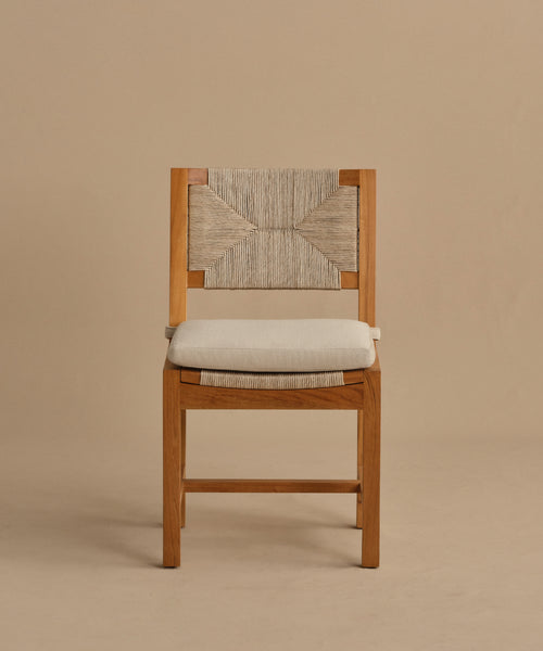 The Outdoor Montecito Dining Chair features a teak frame, a woven geometric backrest, and a light cushioned seat. This durable outdoor piece is shown against a plain beige background.