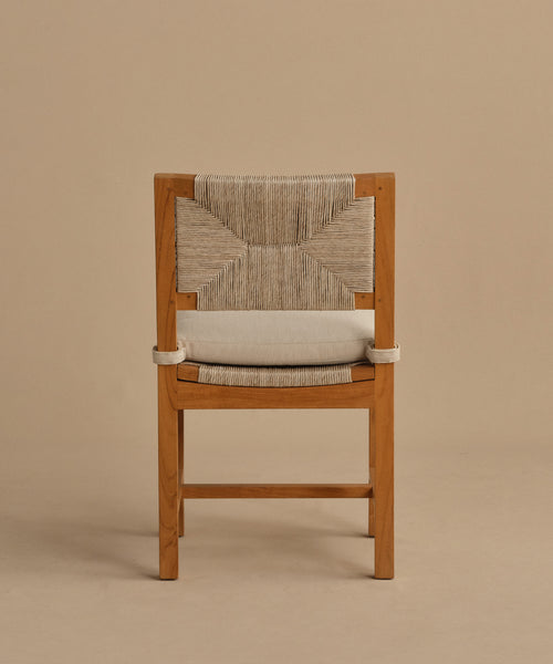 The Outdoor Montecito Dining Chair, made of teak with a natural finish and a woven light-fiber backrest and seat, is presented against a plain beige background—ideal for durable outdoor use.