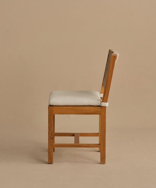 The Outdoor Montecito Dining Chair, made from solid teak with a cushioned seat and backrest in light beige fabric, is shown in profile against a taupe background, highlighting its durable elegance and style.