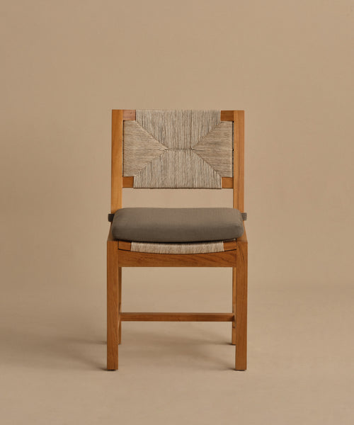 The Outdoor Montecito Dining Chair features a geometric woven ECOLENE backrest, a gray cushioned seat, and a wooden frame, displayed against a plain beige background.