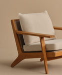 The Outdoor Vista Chair Cushion features beige Italian fabric on a modern wooden armchair with angled legs and a woven backrest, shown against a plain beige background.