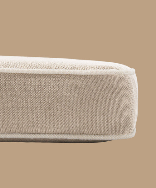 Close-up of the Outdoor Vista Chair Cushion’s edge, showing textured beige Italian fabric and piping, set against a solid light brown background.