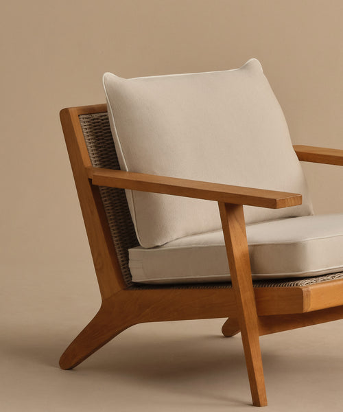 The Outdoor Vista Chair Cushion features beige Italian fabric on a modern wooden armchair with angled legs and a woven backrest, shown against a plain beige background.