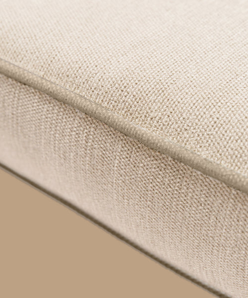 Close-up of the Outdoor Vista Chair Cushion—beige Italian textured fabric with visible edge stitching. From the elegant Vista Collection, perfect for outdoor seating and set against a plain tan background.