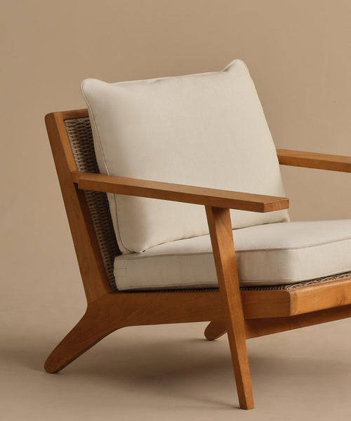 The Outdoor Vista Chair Cushion features cream-colored Italian fabric on a modern wooden armchair with clean lines and minimalist design, shown against a beige background.