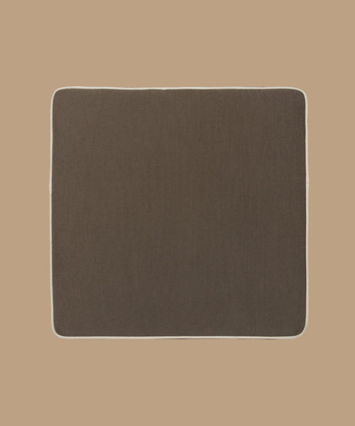The Outdoor Vista Chair Cushion, a square brown mat with rounded corners and white edging, crafted from premium Italian fabric, is shown on a light brown background. From the Vista Collection, it adds style and comfort to any space.