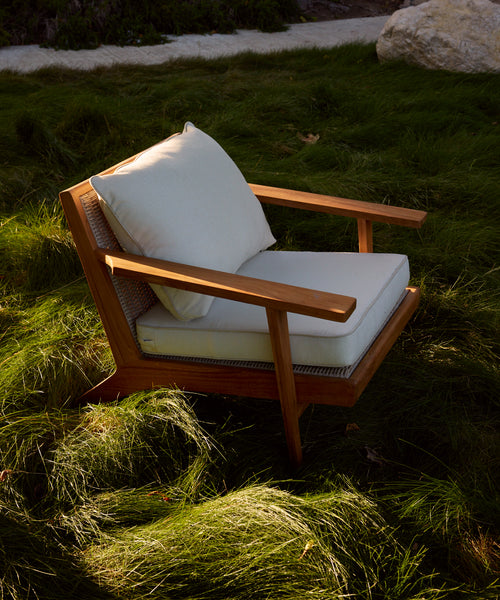 The Outdoor Vista Chair, featuring white Tempotest fabric cushions, is placed on lush green grass outdoors and bathed in natural sunlight.