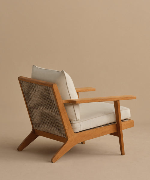 The Outdoor Vista Chair features mid-century modern teak, light beige Tempotest cushions, and a woven ECOLENE seat, showcased against a plain beige background.