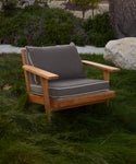 The Outdoor Vista Chair with gray Tempotest fabric cushions is set on green grass among bushes, rocks, and trees in a garden.