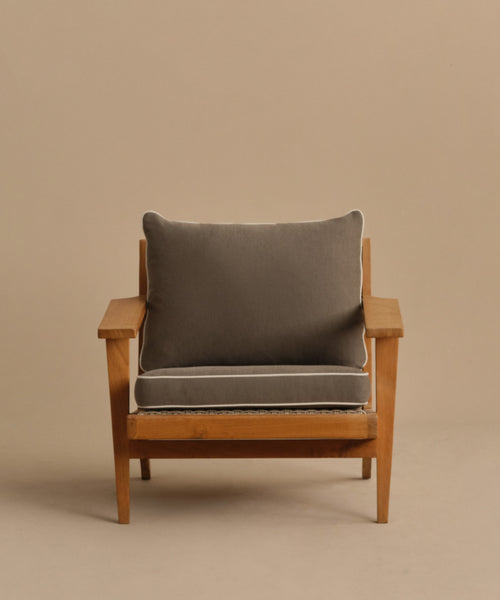 The Outdoor Vista Chair features a wooden teak frame with a thick gray cushion and matching gray backrest, both edged in white piping, shown against a simple beige background.