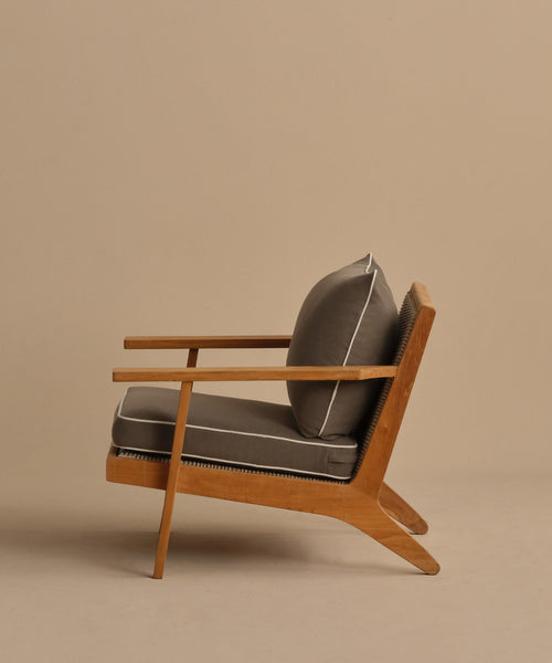 The Outdoor Vista Chair is a modern teak chair with angled legs and armrests, featuring thick gray Tempotest fabric cushions with white piping, shown against a plain beige background.