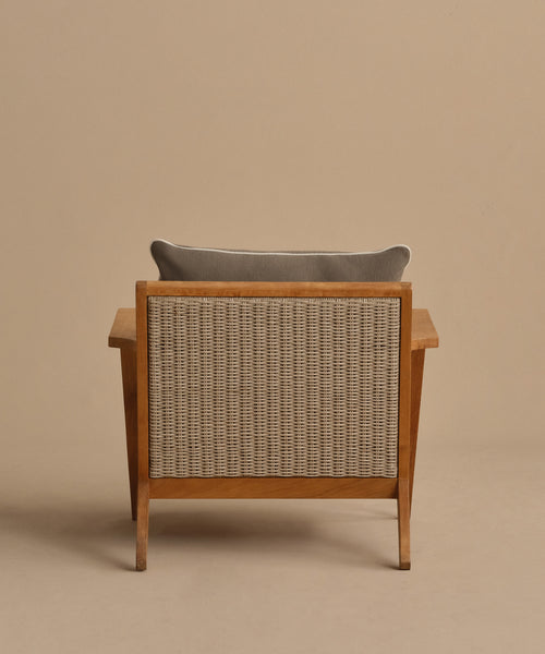 The Outdoor Vista Chair features a wooden frame, woven rattan backrest, and gray Tempotest cushion, set against a beige background—an elegant choice for outdoor seating.