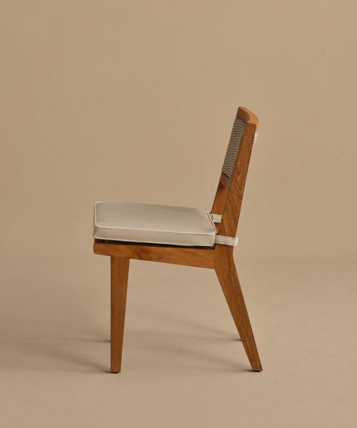 The Outdoor Vista Dining Chair is a minimalist, modern piece crafted from solid teak with a woven backrest and light beige cushion, displayed in profile against a plain beige background.