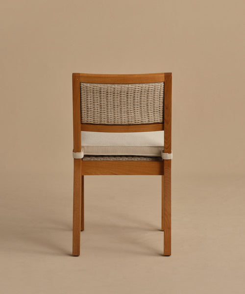The Outdoor Vista Dining Chair, made of solid teak with a woven ECOLENE rattan backrest and a light cushioned seat, is shown from behind against a plain beige background.