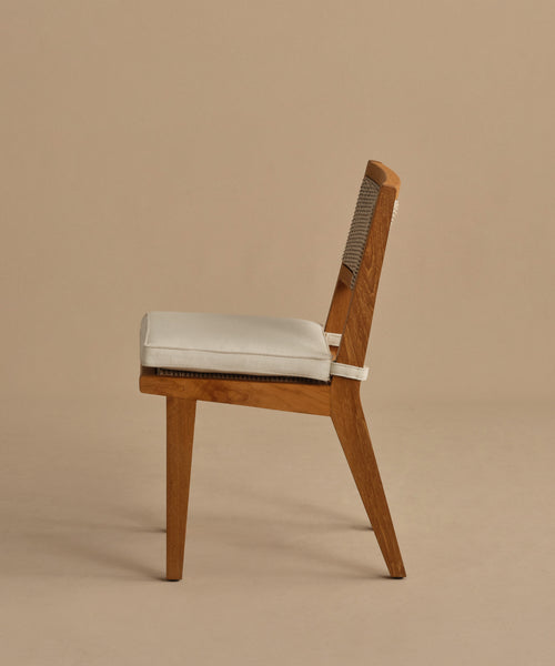 Side view of the Outdoor Vista Dining Chair in solid teak with a beige cushioned seat and ECOLENE woven backrest, shown against a plain beige background. Its minimalist, modern design makes it ideal for outdoor dining spaces.