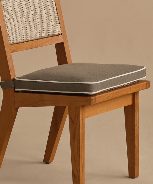 The Outdoor Vista Dining Chair features a solid teak frame, a woven ECOLENE backrest, and a gray seat cushion with white piping, shown against a neutral beige background.