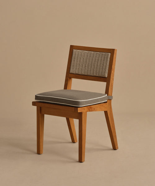 The Outdoor Vista Dining Chair features solid teak, a woven ECOLENE backrest, and a gray seat cushion. With angled legs and a modern design, it stands against a plain beige background.