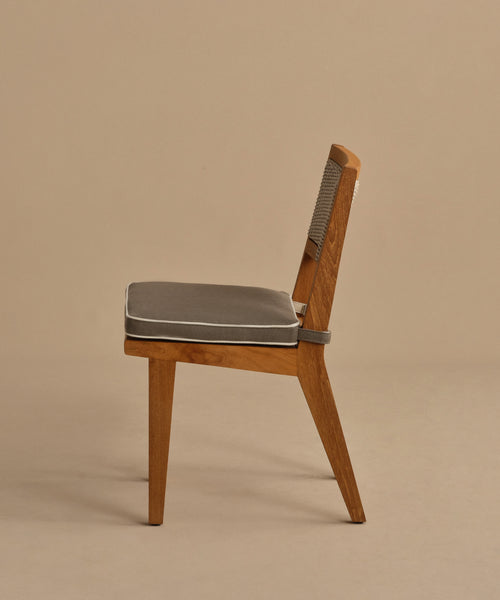 Side view of the Outdoor Vista Dining Chair in solid teak with a grey cushioned seat, angled backrest, and ECOLENE woven detail on the upper back, set against a plain beige background.