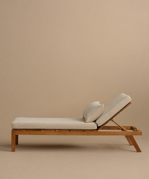 The Outdoor Vista Lounge Cushion, featuring luxurious beige Italian fabric and an adjustable backrest, is displayed on a modern wooden chaise lounge against a plain light brown background.
