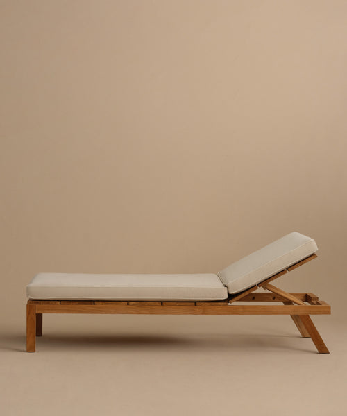 The Outdoor Vista Lounge Chair features a teak frame and light beige cushions on the seat and backrest, set against a plain beige background—ideal for anyone seeking durable outdoor furniture.