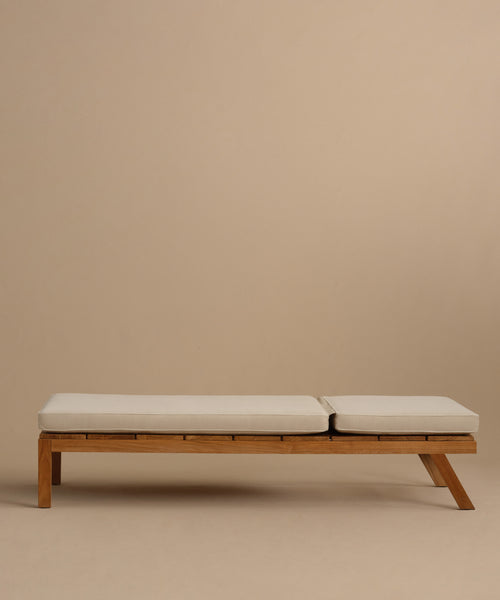 The Outdoor Vista Lounge Chair, featuring clean lines and a minimalist teak frame with light-colored seat cushions, is showcased against a plain beige background, highlighting its modern design and durable appeal for outdoor living.