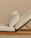 A close-up side view of the Outdoor Vista Lounge Chair, featuring cream-colored cushions and a matching pillow, set against a plain beige background.