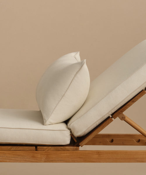 A close-up side view of the Outdoor Vista Lounge Chair, featuring cream-colored cushions and a matching pillow, set against a plain beige background.