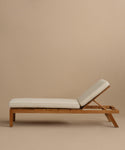 The Outdoor Vista Lounge Chair is a wooden outdoor lounge chair with light beige cushions and an adjustable backrest, designed for durability and shown against a plain beige background.