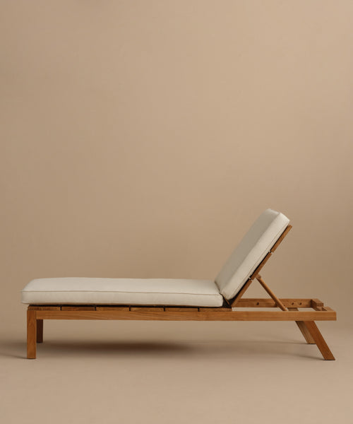 The Outdoor Vista Lounge Chair, featuring a teak frame, light beige cushion, and adjustable backrest, is shown in profile against a plain beige background to highlight its elegant and durable lounge design.