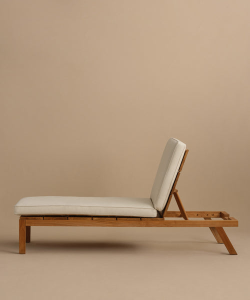 The Outdoor Vista Lounge Chair features a teak frame, light cushion, and adjustable backrest. Photographed against a beige background, it highlights minimalist style and durable outdoor design.