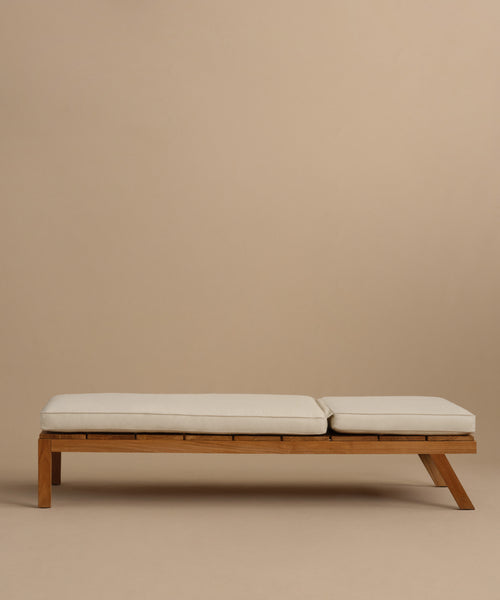 The Outdoor Vista Lounge Chair, a minimalist wooden seat with two cream cushions, sits against a plain beige background, embodying the simple and modern design of durable outdoor furniture.