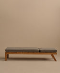 The Outdoor Vista Lounge Chair is a minimalist wooden daybed with two gray cushions, set against a plain beige background. Its simple, modern form and slightly elevated side are inspired by the timeless outdoor lounge chair design.